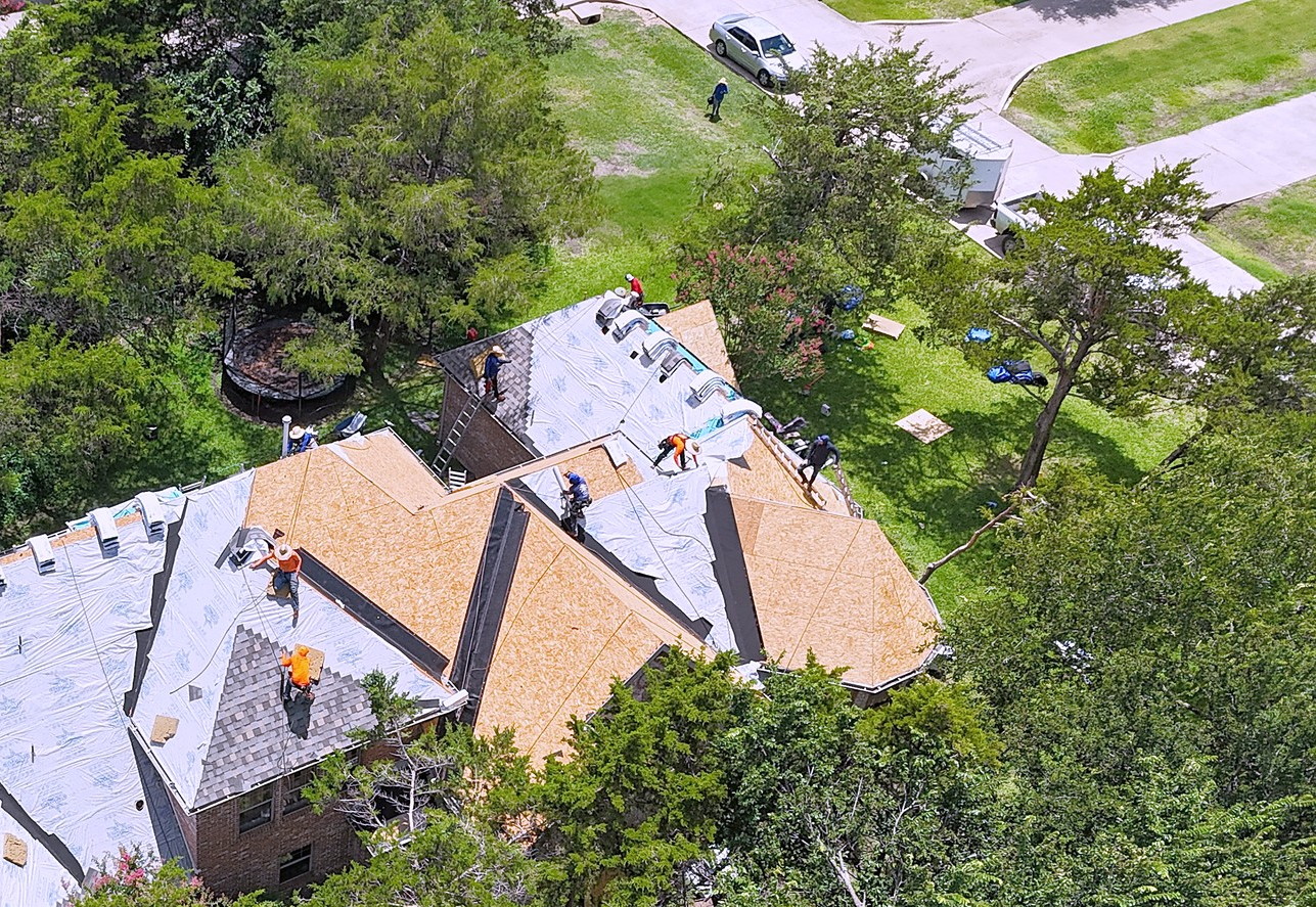 A crew working on a roof, part shingled and part underlayment