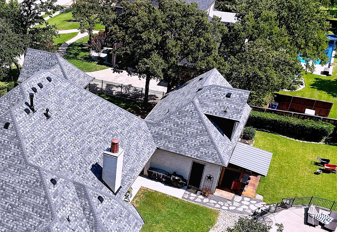 A large brick home with a new grey shingle roof, seen from the air