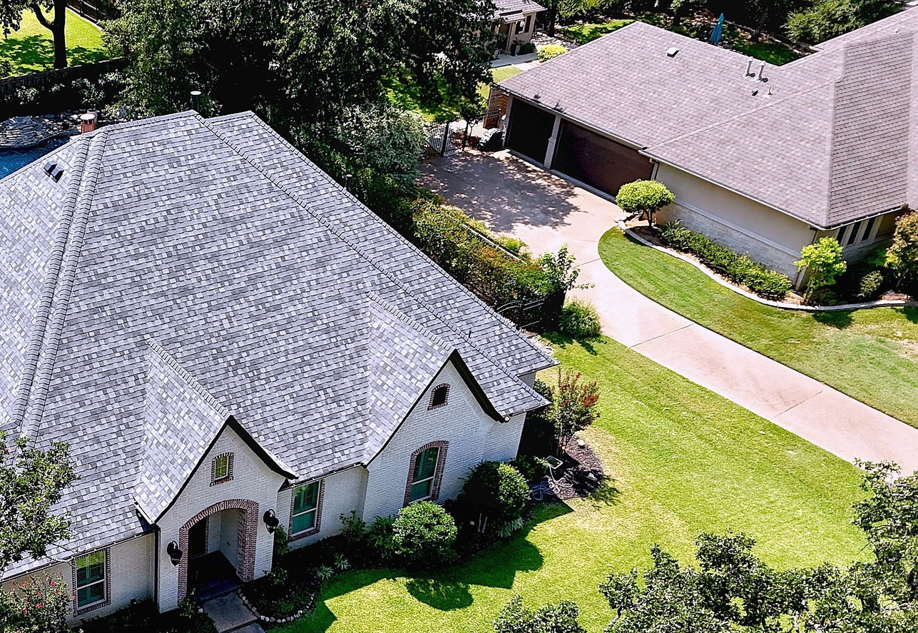 A French country style home with a new light grey shingle roof, seen from the air