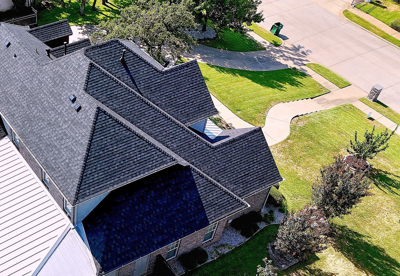 A home with a dark shingle roof beside a standing seam metal patio roof