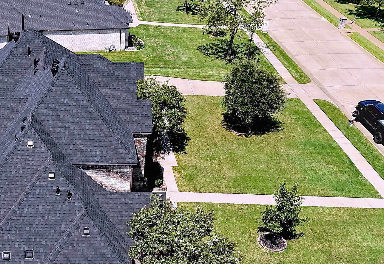 A brick home with a new dark shingle roof beside a curved swimming pool