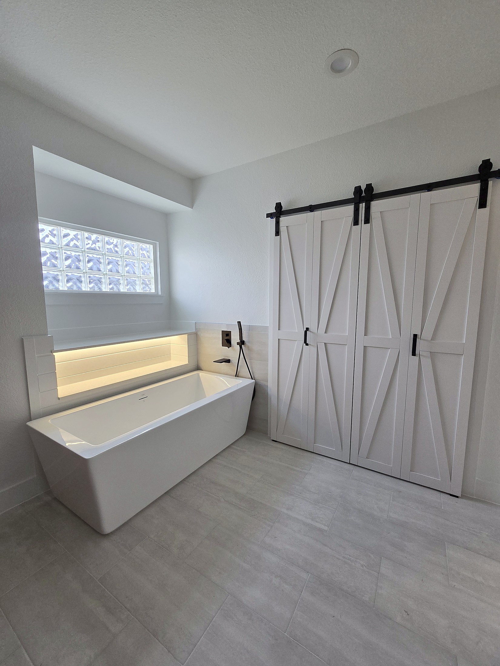 A remodeled bathroom with a freestanding tub, a lit niche and barn doors