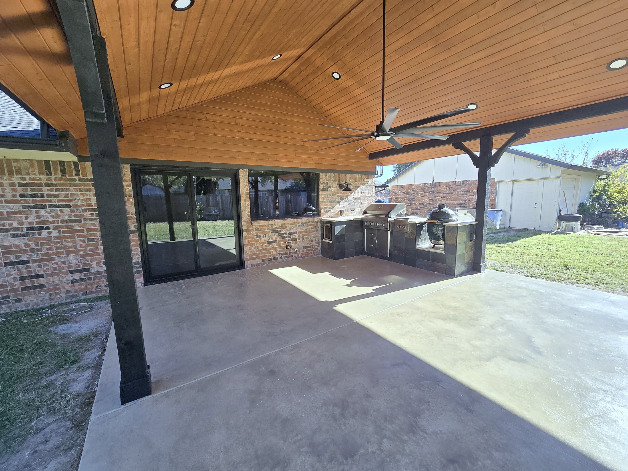A covered patio with a stained cedar ceiling and a built in outdoor kitchen